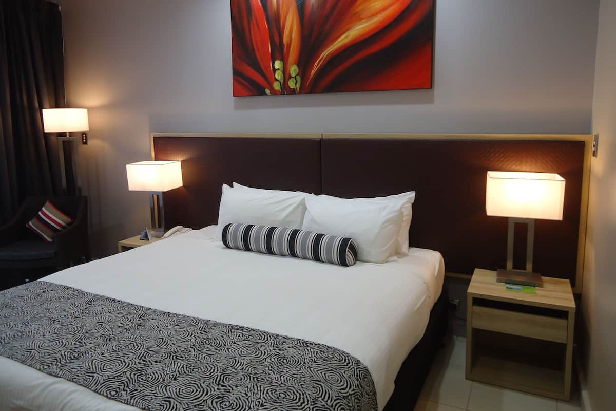 Une chambre d’hôtel avec un grand lit, deux lampes de chevet, un oreiller à rayures, une tête de lit et un tableau au mur.