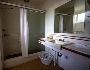Un baño con ducha, lavamanos, espejo y una cesta blanca.