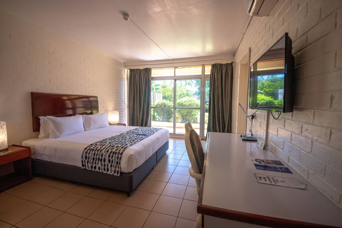 Une chambre d’hôtel avec un lit, un bureau, une chaise, une télévision et une fenêtre avec des rideaux.