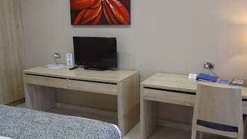 Een hotelkamer met een bed, een bureau met een televisie, een stoel en een groot bloemenportret aan de muur.