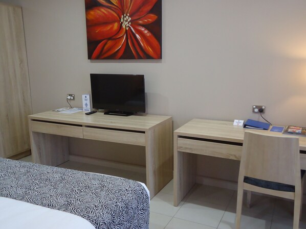Une chambre d’hôtel avec un lit, un bureau avec une télévision, une chaise et un grand tableau représentant des fleurs accroché au mur.