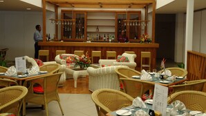 Ein Restaurant mit Korbmöbeln, einer Bar mit Flaschen und Gläsern sowie eine Person, die an der Bar steht.