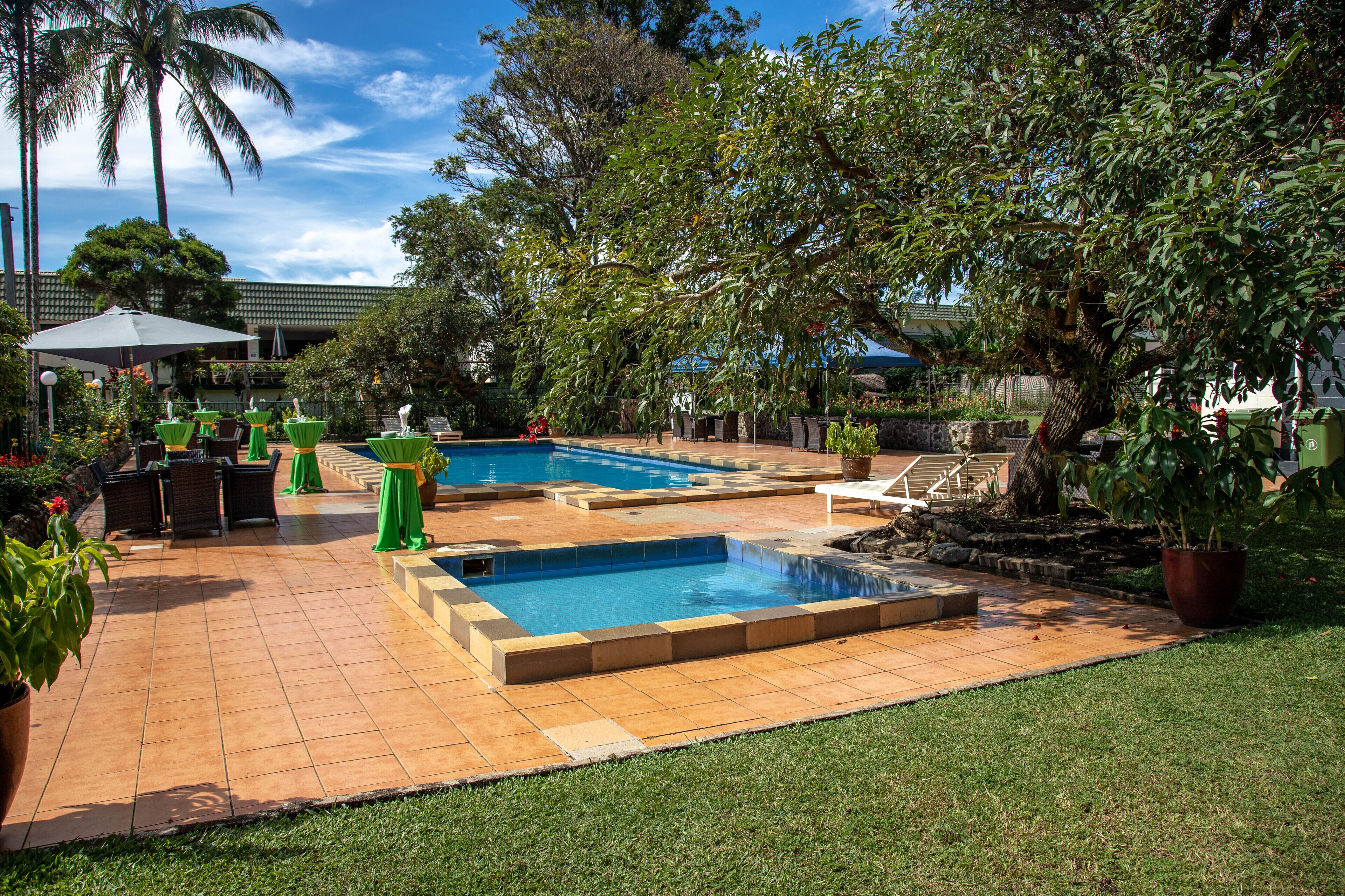 Un jardin avec une piscine, des chaises vertes et des plantes en pot.