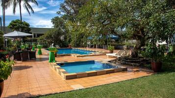 Un jardin avec une piscine, des chaises vertes et des plantes en pot.