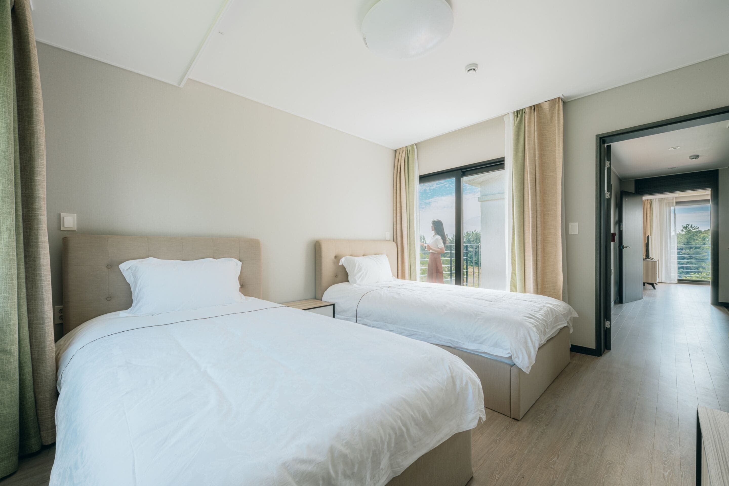 A hotel room with two beds, a large window, and a view of the outdoors.