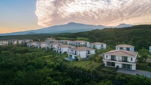 Un barrio residencial con casas modernas, rodeado de abundante vegetación y montañas al fondo.