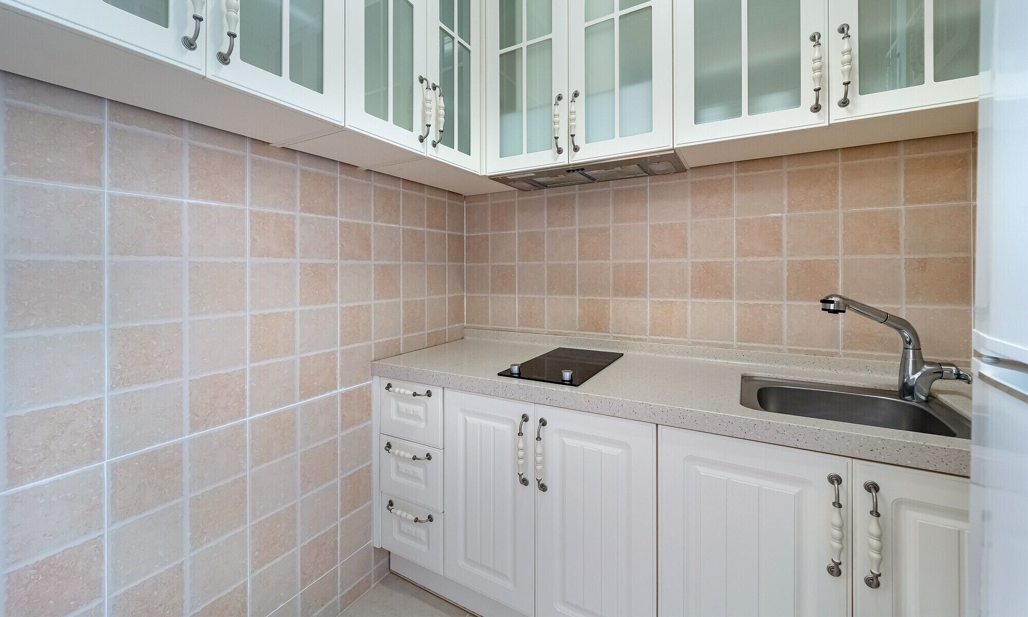 A kitchen with white cabinets, a stainless steel sink, and beige tiles.