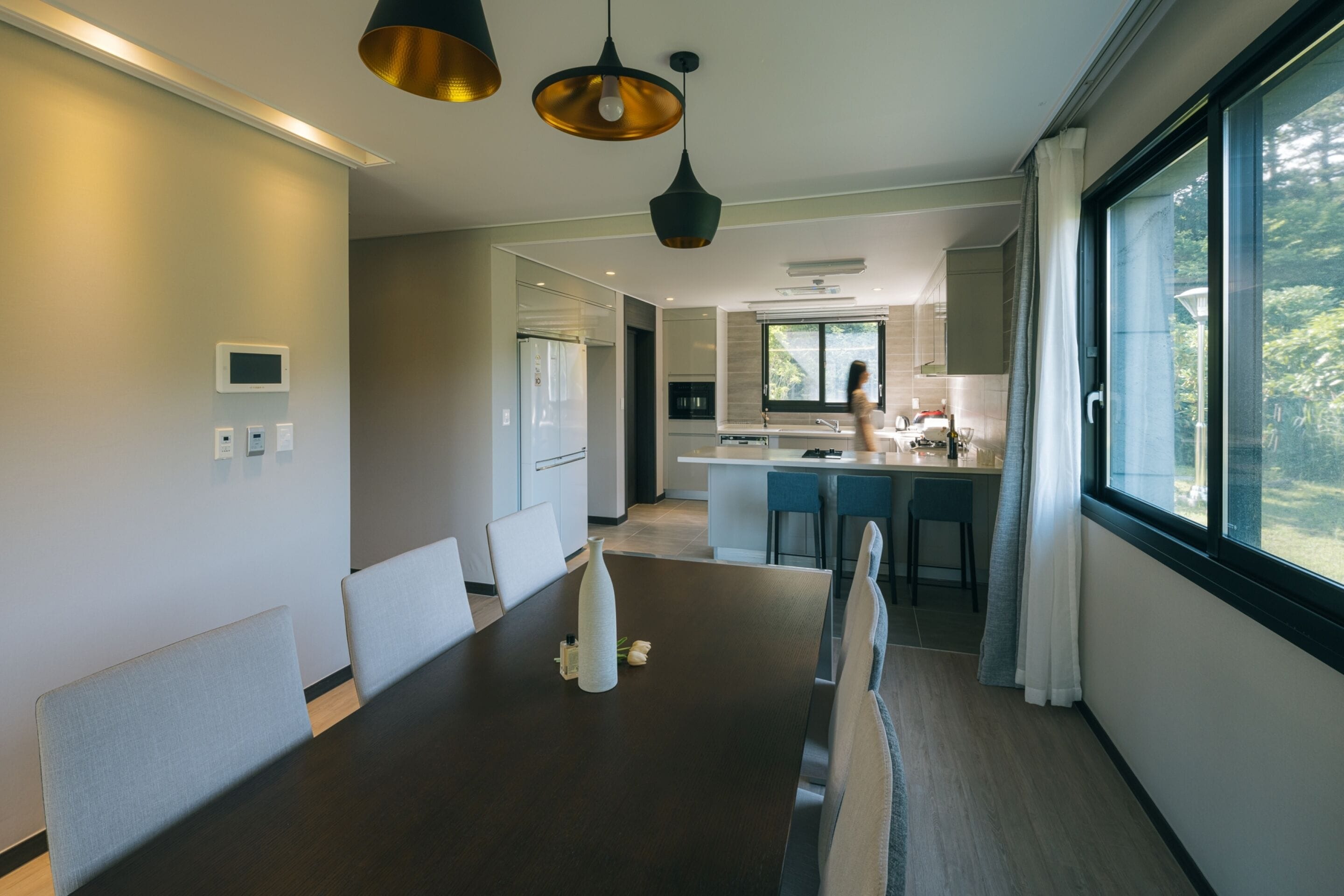 A modern dining area with a dark wooden table, light grey upholstered chairs, and pendant lighting.