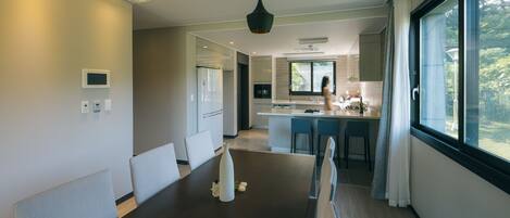 A modern dining area with a dark wooden table, light grey upholstered chairs, and pendant lighting.