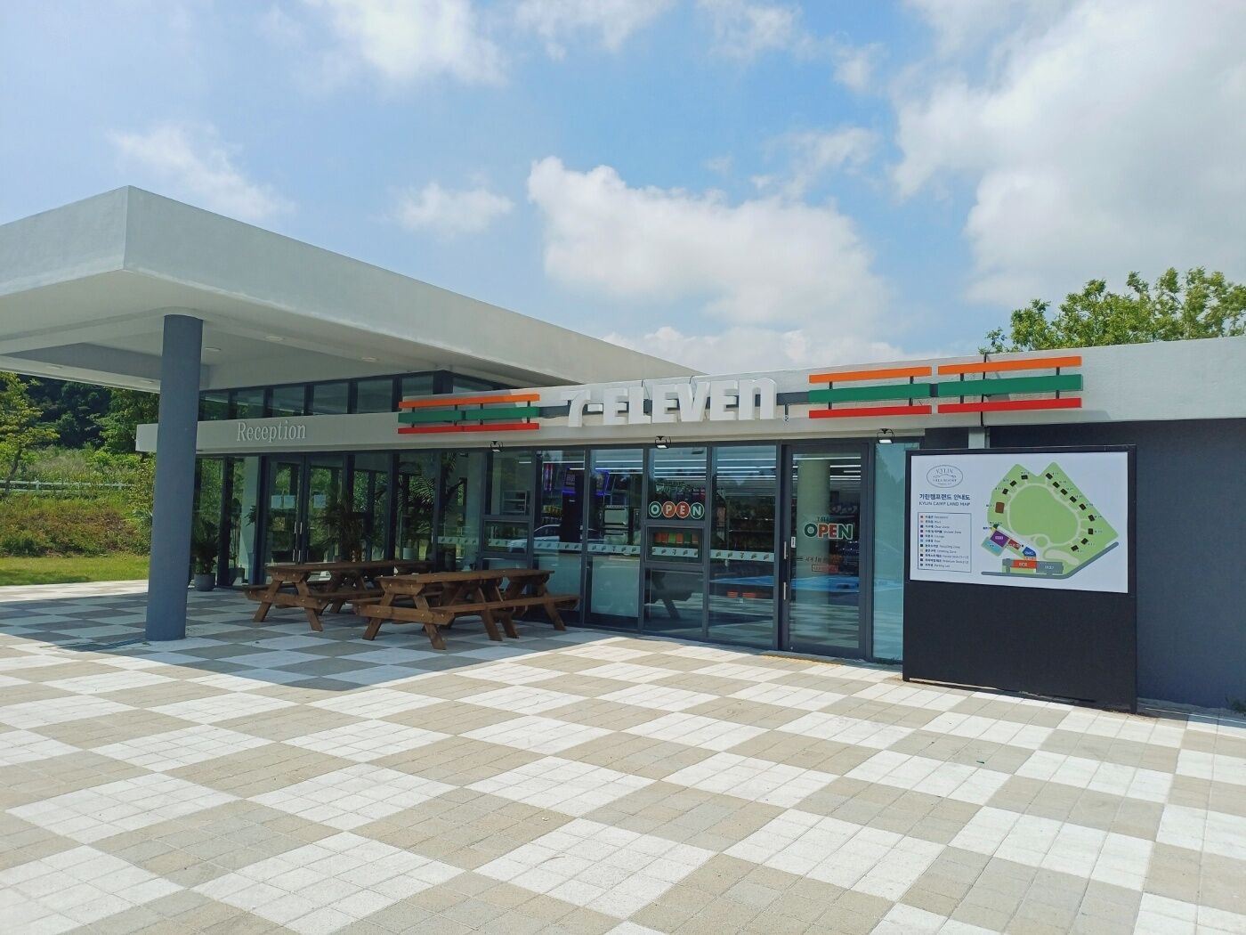 Una tienda 7-Eleven con zona de recepción, mesas al aire libre y aparcamiento.