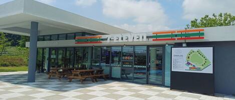 Una tienda 7-Eleven con zona de recepción, mesas al aire libre y aparcamiento.