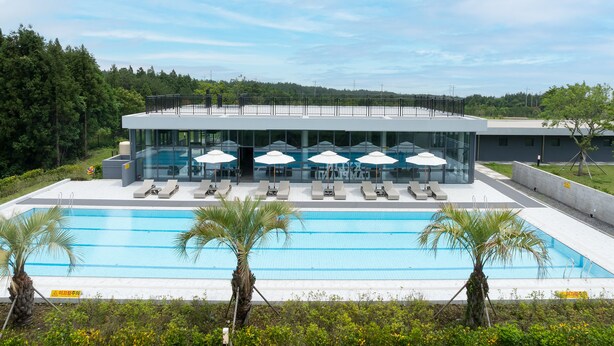 Un hotel moderno con una piscina grande, tumbonas y sombrillas.