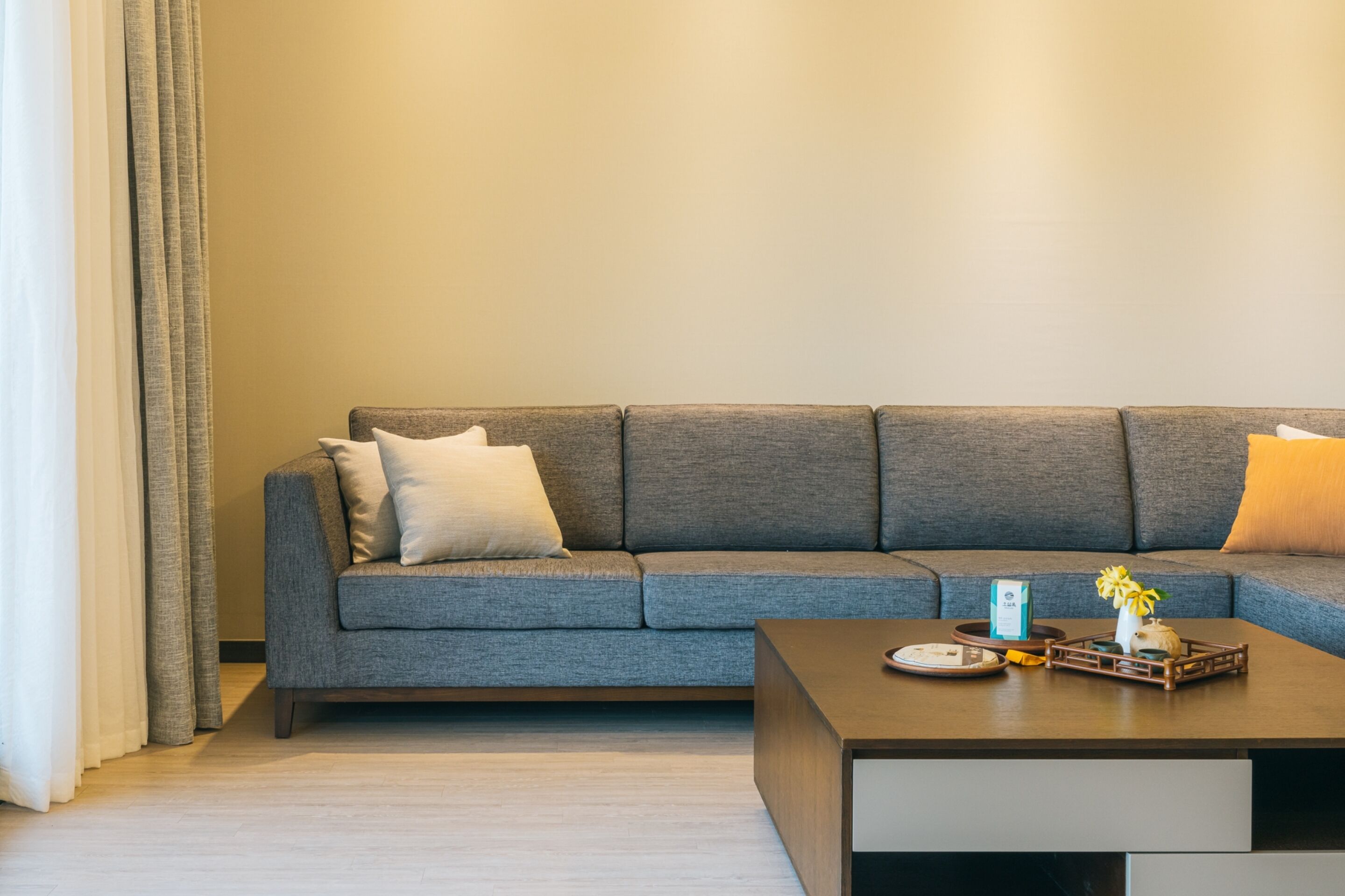 A modern living room with a grey sectional sofa, a wooden coffee table, and a vase with flowers.