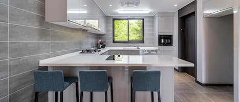 Una cocina moderna con una isla central, taburetes de bar, una ventana y electrodomésticos integrados.