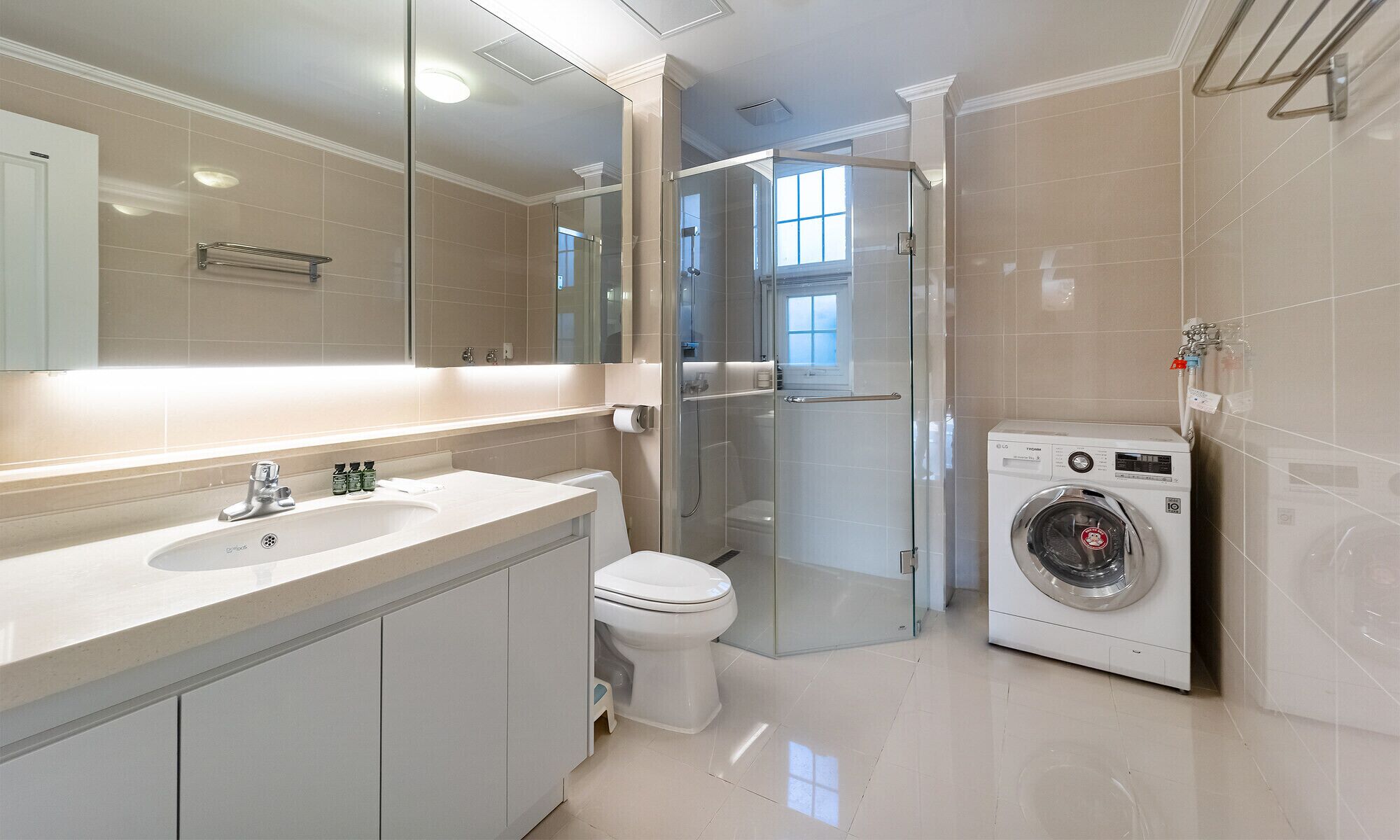 A modern bathroom with a large mirror, a sink, a toilet, a glass shower enclosure, and a washing machine.