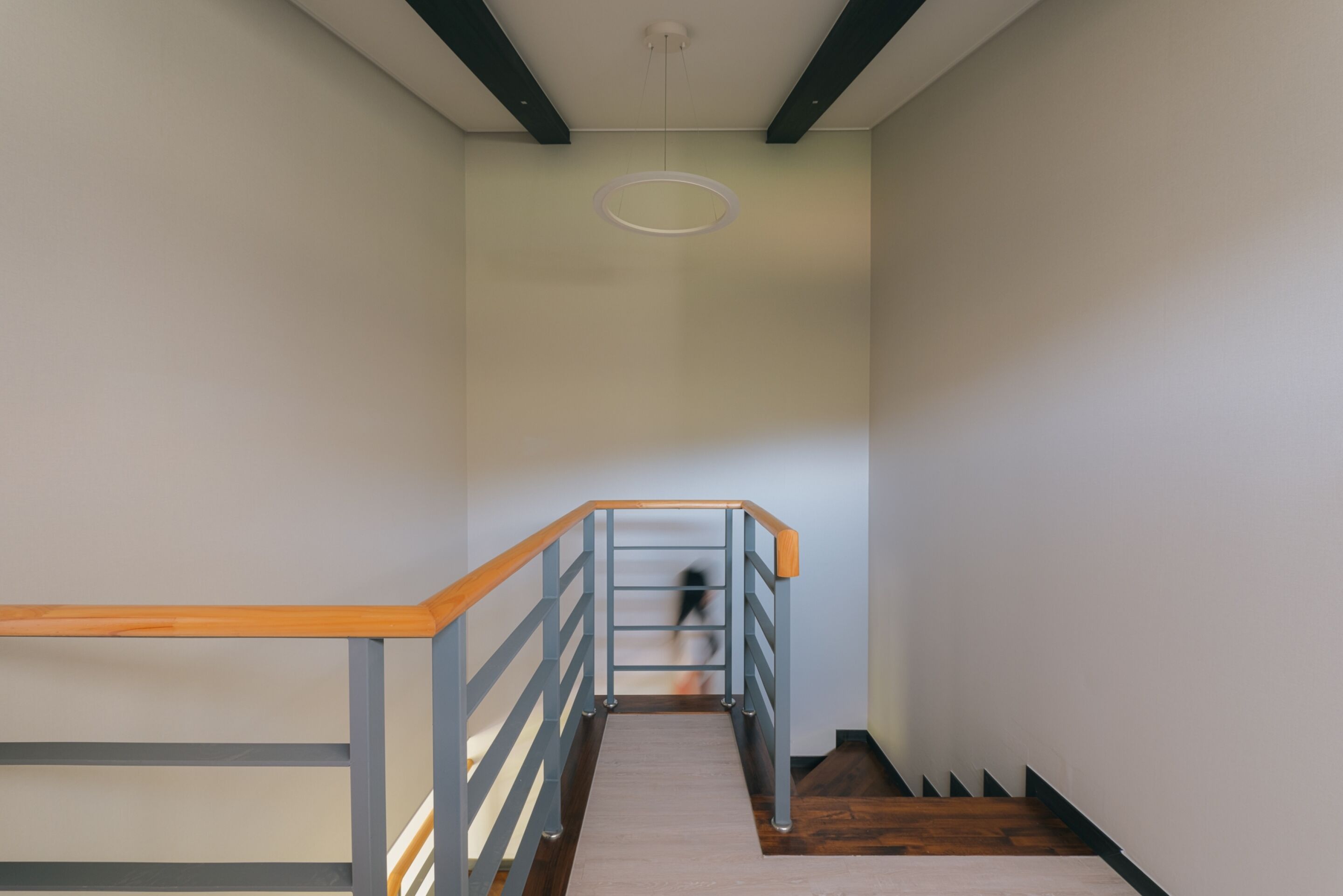 A staircase with wooden handrails and a grey metal railing, leading to a landing with a circular light fixture.