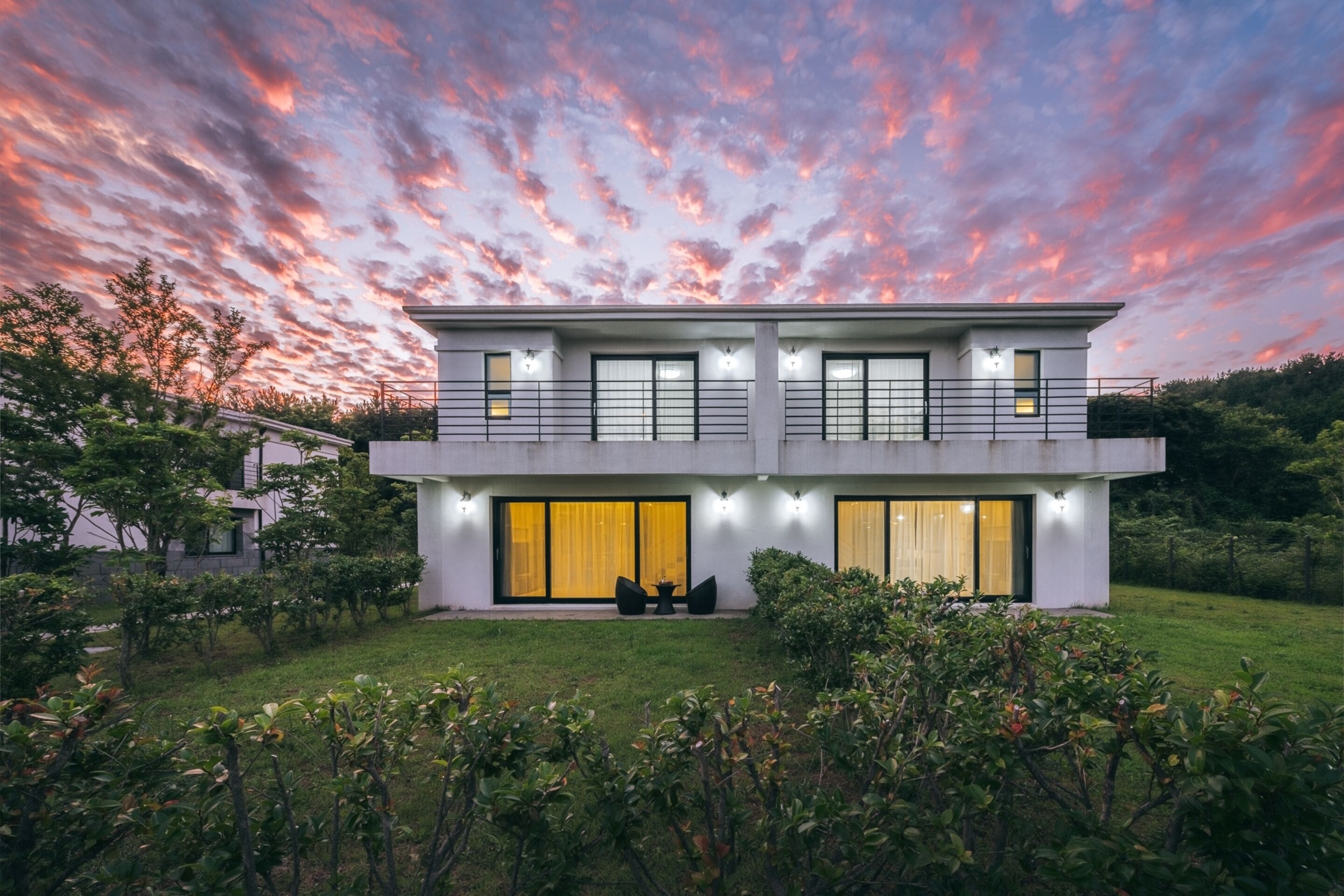 Una casa moderna de dos plantas con ventanas amplias, un balcón y un jardín bien cuidado.