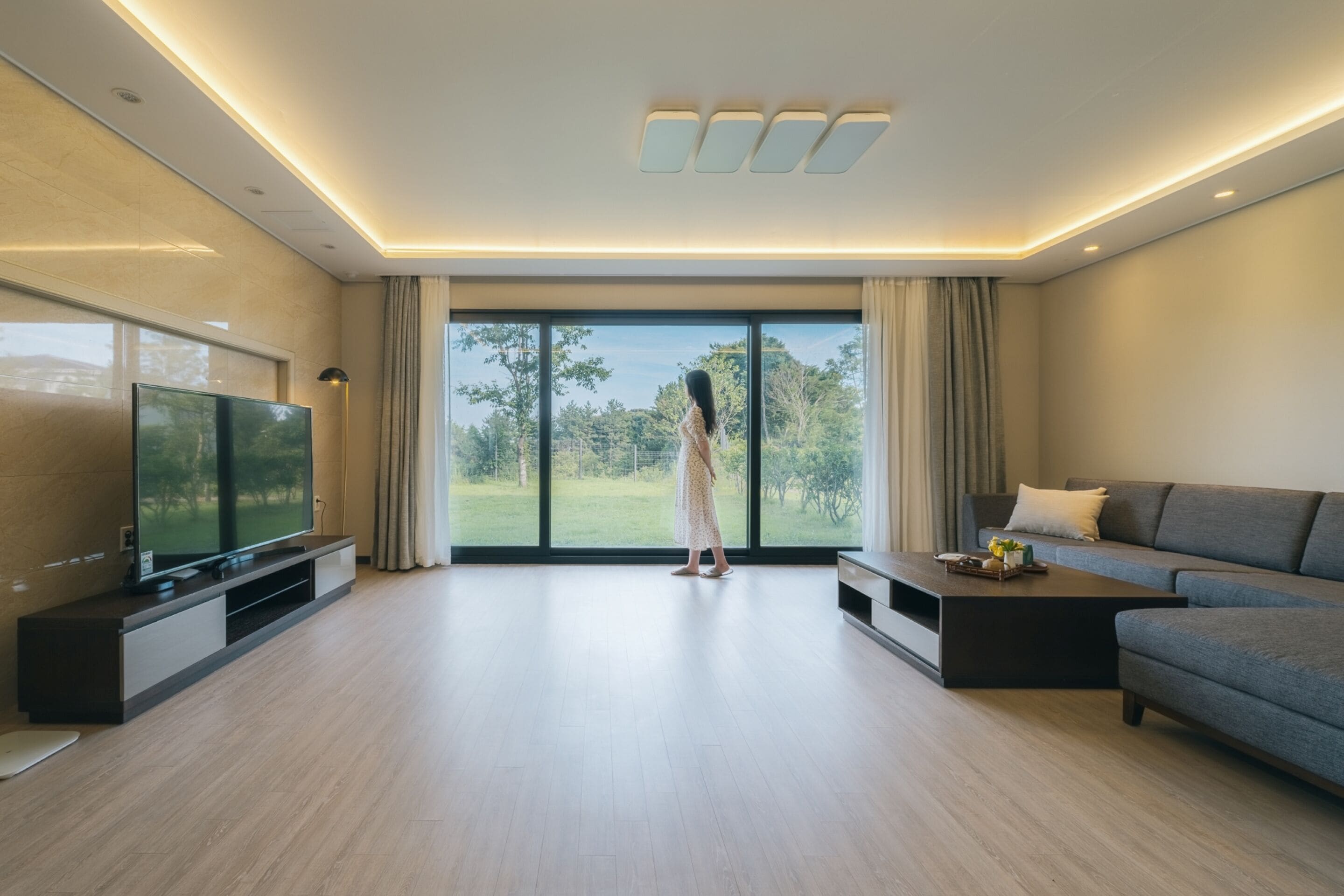 Uma sala de estar moderna com uma televisão de tela plana grande, um sofá cinza e uma mesa de centro.