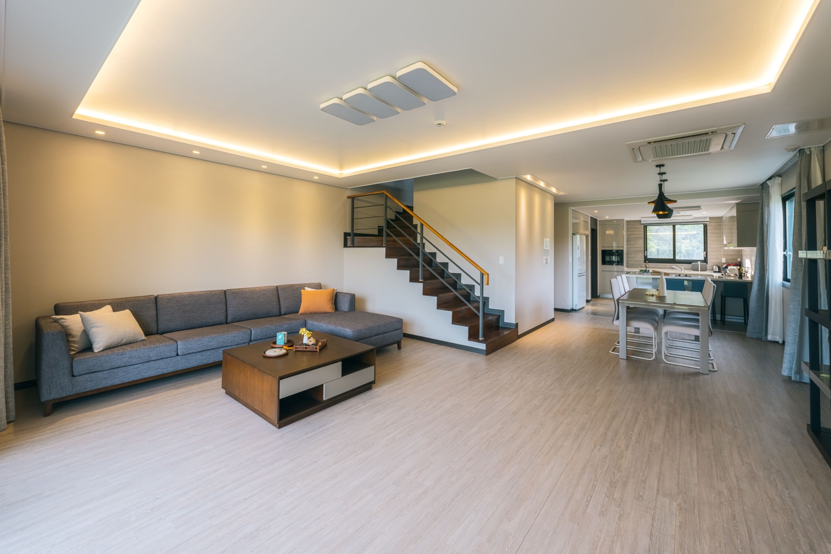 A modern living room with a grey sofa, wooden coffee table, and a staircase leading to a kitchen area.