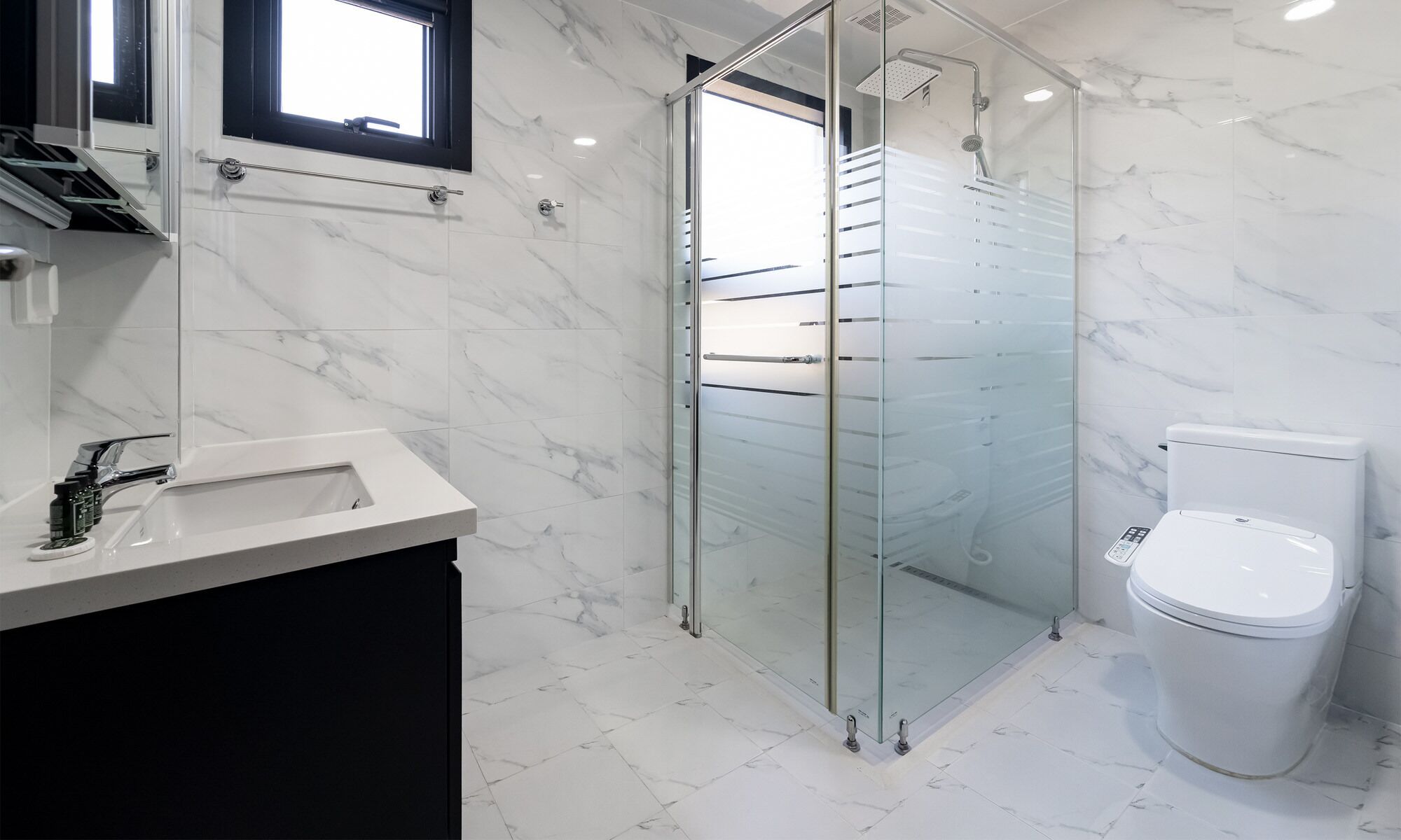 Un baño moderno con ducha acristalada, inodoro blanco y suelo de mármol.