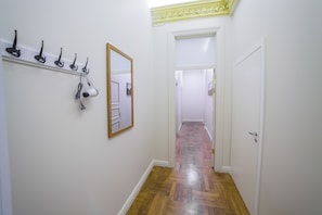 Un couloir avec un plancher en bois, des murs blancs et un miroir sur le côté gauche.