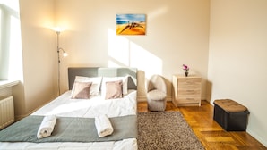 A neatly arranged bedroom with a bed, bedside lamp, a small table with a vase, a chair, and a bench. - Mosaic Center Apartments (Riga)