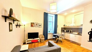 A compact living space with a sofa, a TV, a dining table with chairs, a kitchen area, and a window with curtains. - Mosaic Center Apartments (Riga)