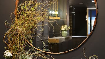 A mirror with a wooden frame reflecting a chandelier and two vases with white flowers on a wooden shelf.