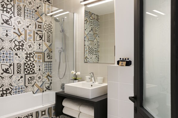 A modern bathroom with patterned tiles, a white sink, and a glass-enclosed shower. - Hotel Square Louvois (Paris)