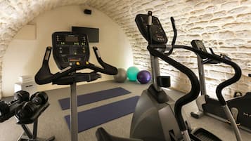 A gym with exercise equipment, a stone wall, and a small TV screen.