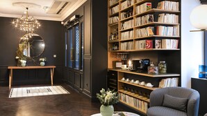 A cozy reading area with a large bookshelf, a comfortable armchair, and a small table with a vase of flowers. - Hotel Square Louvois (Paris)