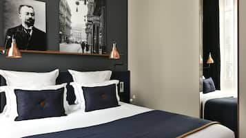 A neatly made bed with white and navy bedding, two wall-mounted lamps, and a framed picture above the bed.