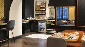 A modern hotel room with a kitchen area, a dining table set for breakfast, and a large mirror reflecting the room. - Hotel Square Louvois (Paris)
