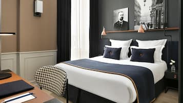 A neatly arranged hotel room with a large bed, a bedside table, a chair, and a desk.