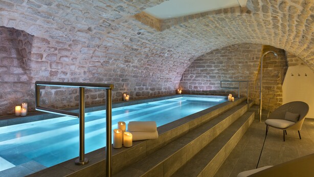A stone-walled spa area with a large soaking tub, candles, and a modern chair. - Hotel Square Louvois (Paris)