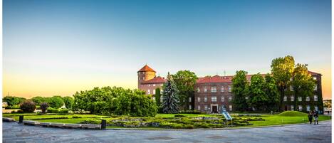 A historic building with a tower, surrounded by well-maintained gardens and a paved plaza.