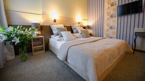 A hotel room with a large bed, bedside tables, a TV, and a vase of flowers. - Hotel Kazimierz III (Kraków)