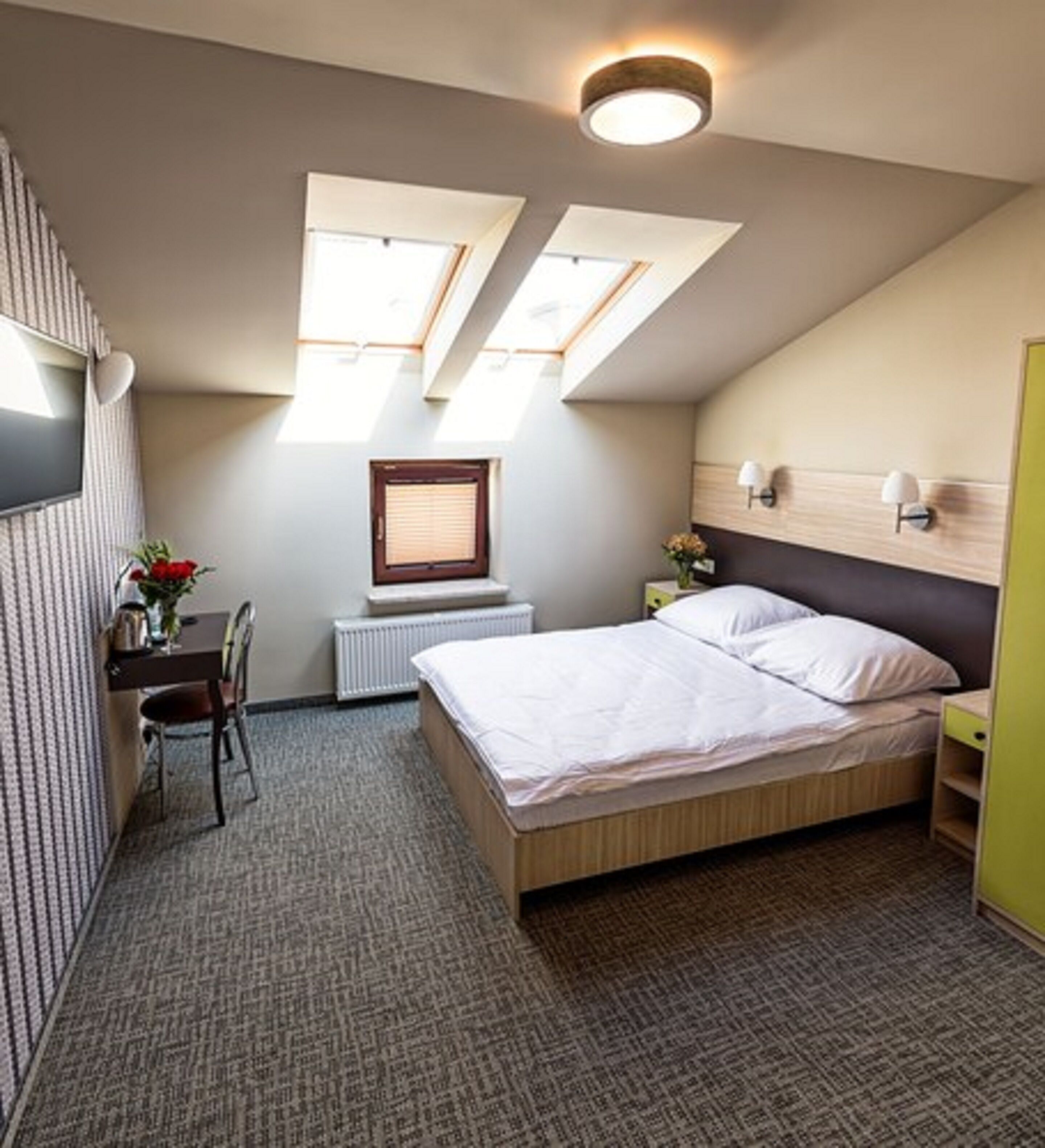 A bedroom with a bed, a desk, a chair, a radiator, and two skylights.