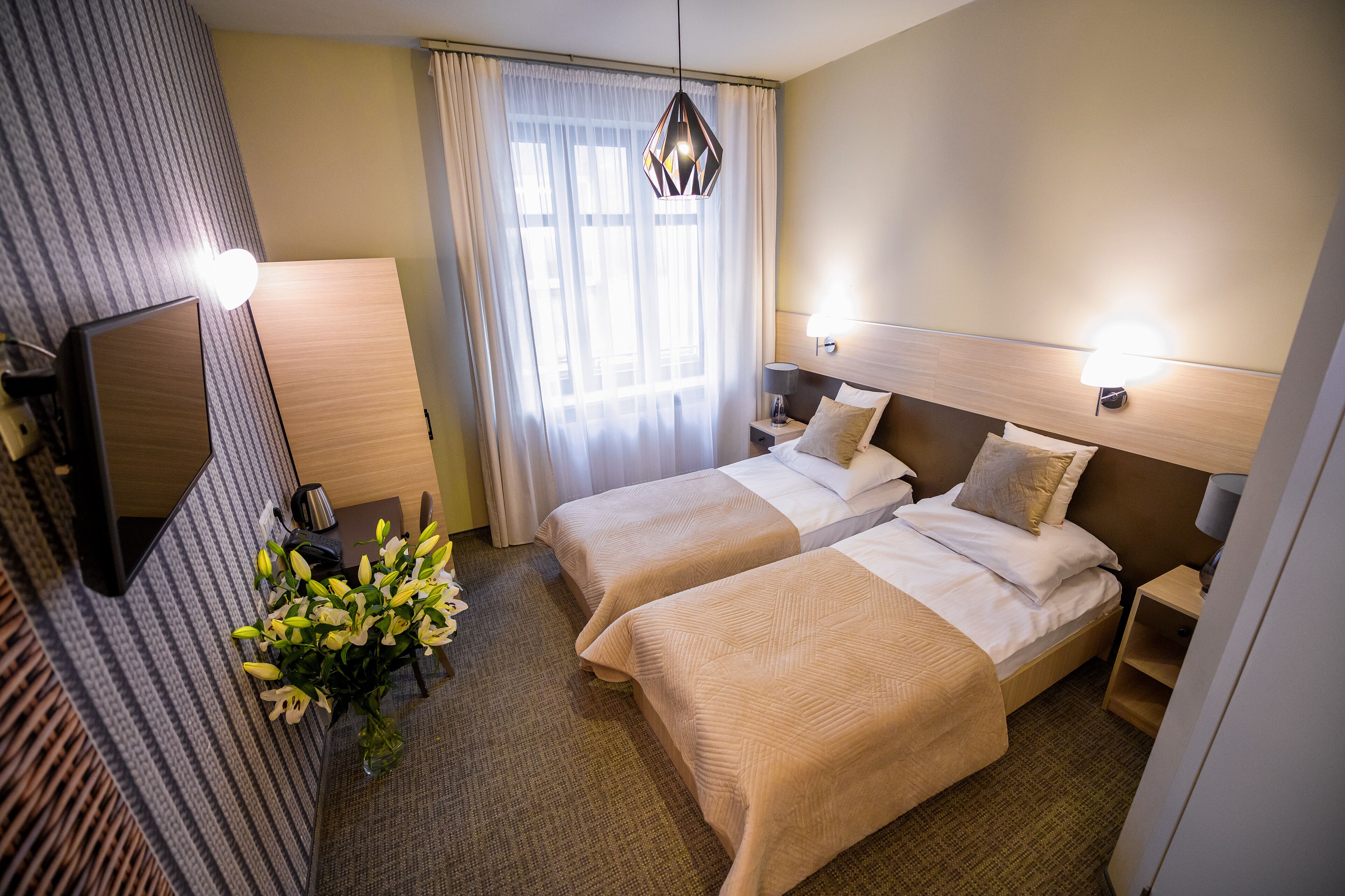 Habitación de hotel con dos camas, un espejo grande, un escritorio con lámpara y una ventana con cortinas.