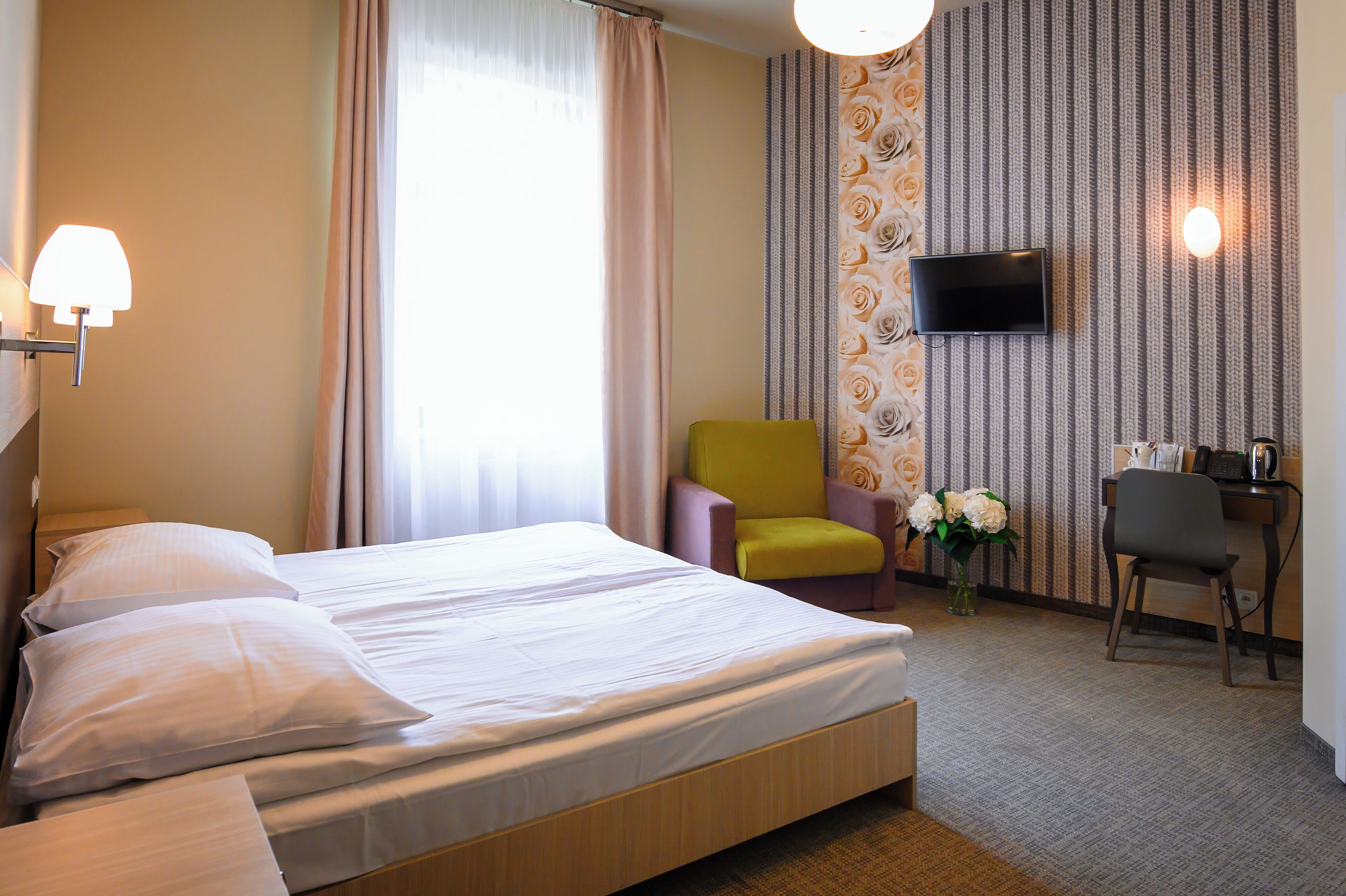 Une chambre d’hôtel avec un lit, un bureau, une chaise, une télévision et une fenêtre avec des rideaux.