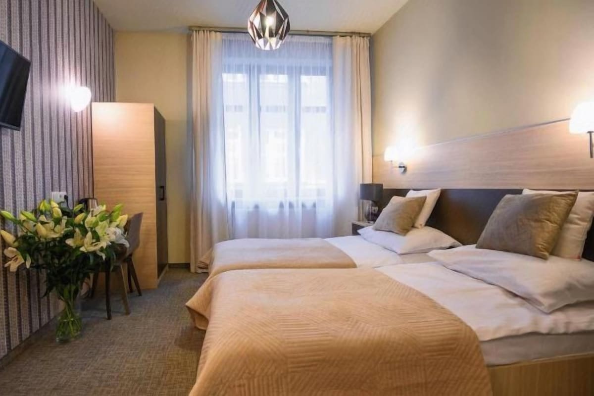 A hotel room with a large bed, a TV mounted on the wall, a desk with a chair, and a vase of flowers.