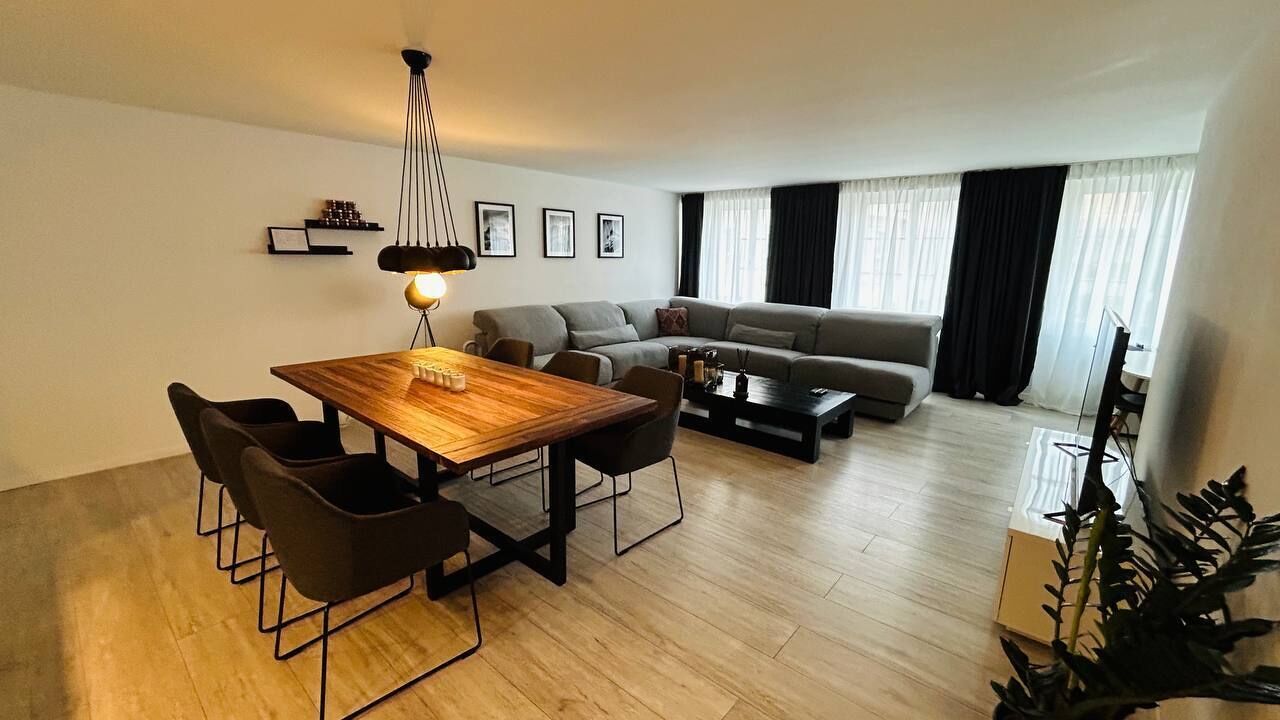 Un salón moderno con una mesa de comedor de madera, sillas negras, un sofá gris y una mesa de centro.