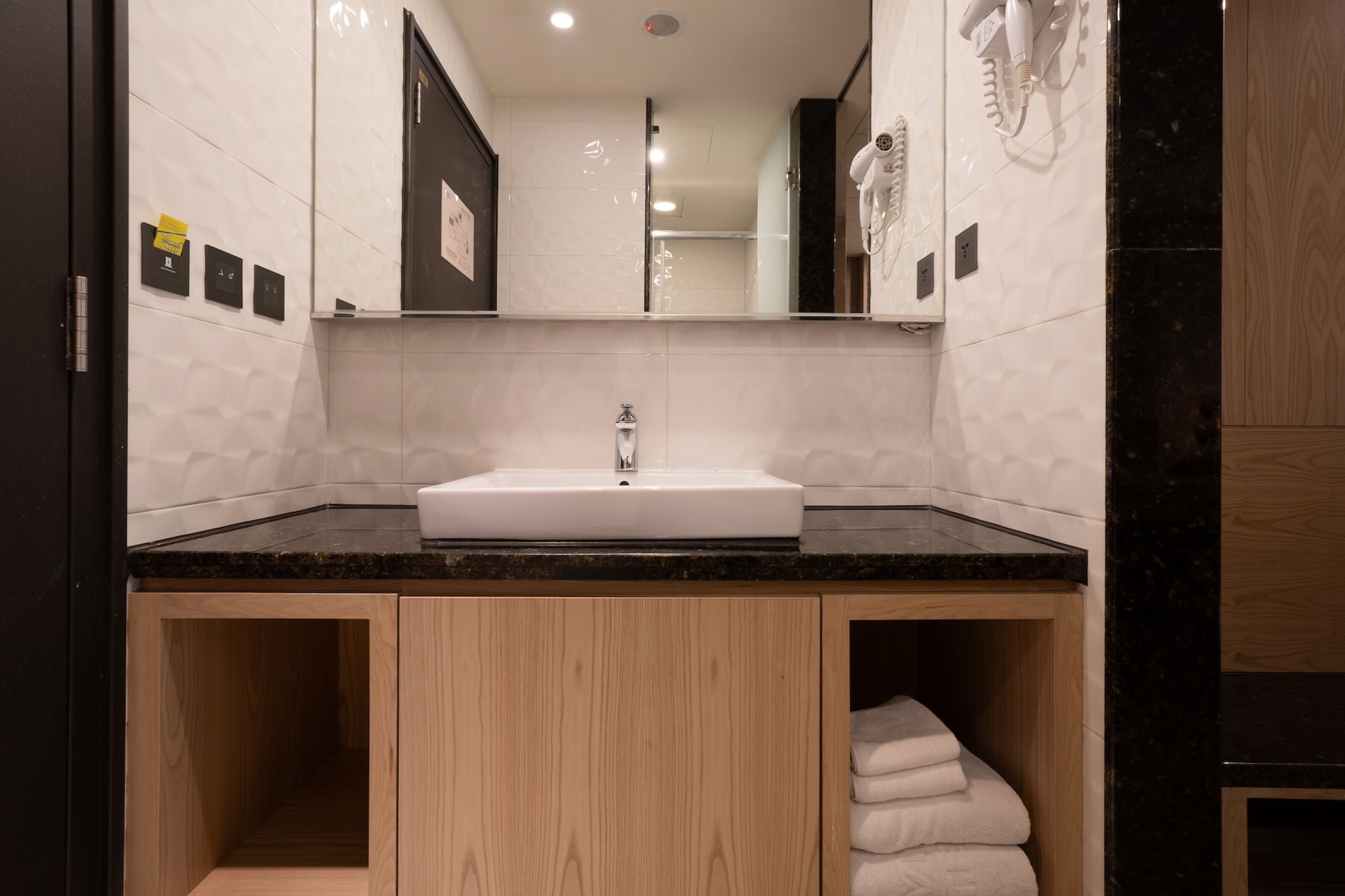 Ein modernes Badezimmer mit einem weißen Waschbecken, Holzschränken und einem großen Spiegel.