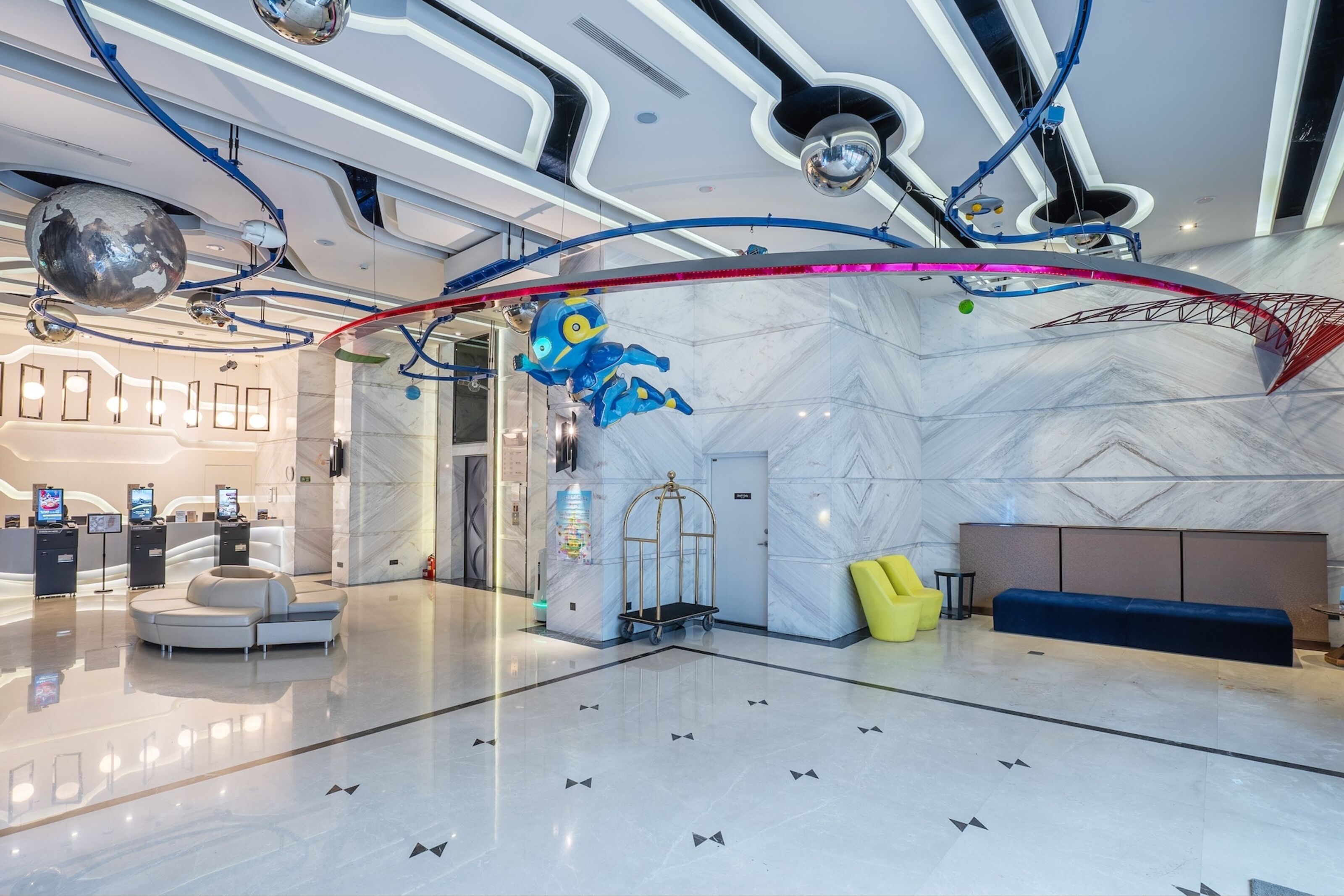 A modern lobby with a marble floor, a reception desk, a blue robot decoration, and a yellow chair.