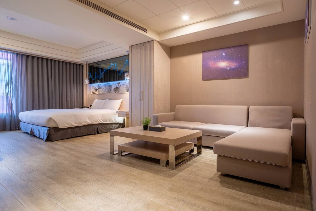 A modern hotel room with a bed, a sofa, a coffee table, and a wall-mounted galaxy artwork.