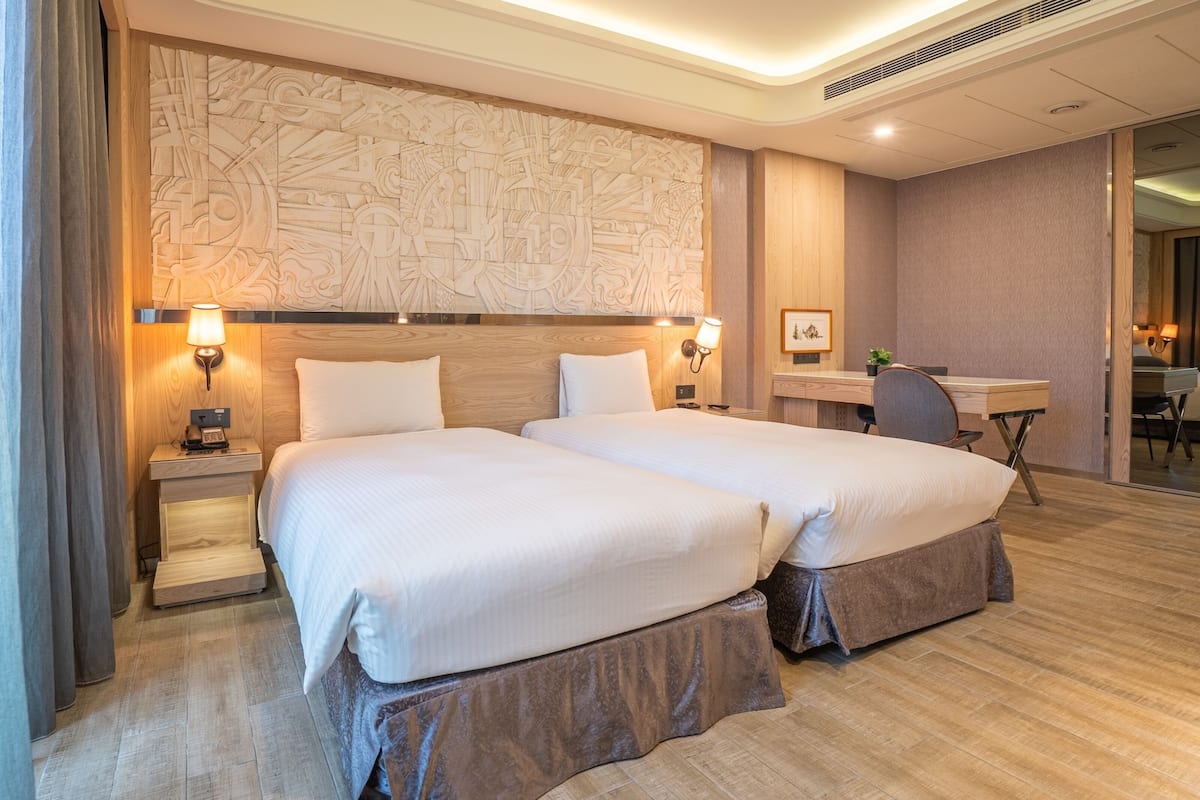 A hotel room with two beds, a desk, and a chair.
