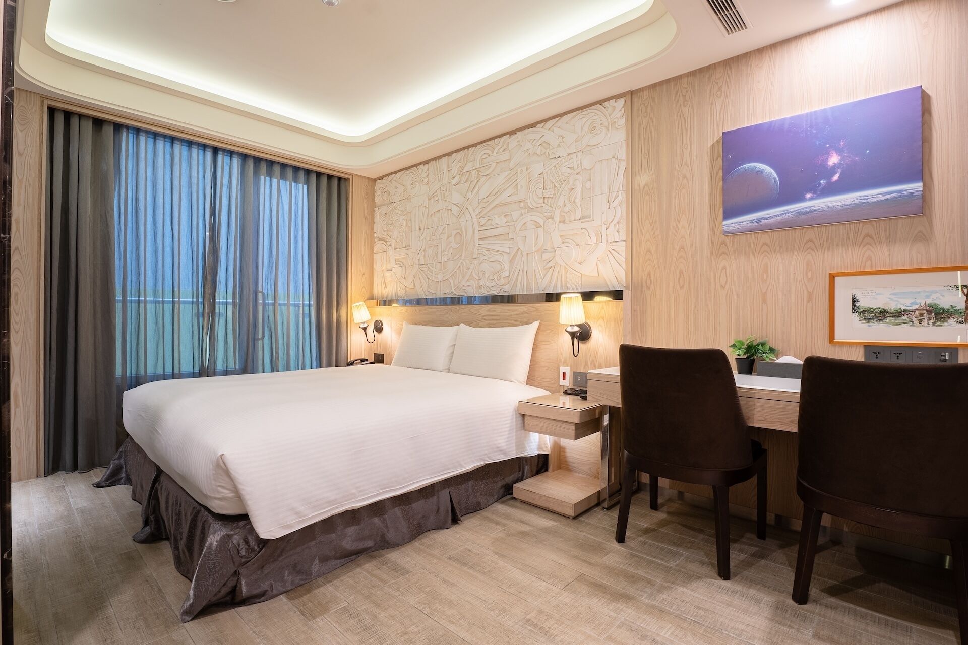 Une chambre d’hôtel avec un grand lit, un bureau avec deux chaises, un téléviseur fixé au mur et une fenêtre avec des rideaux.