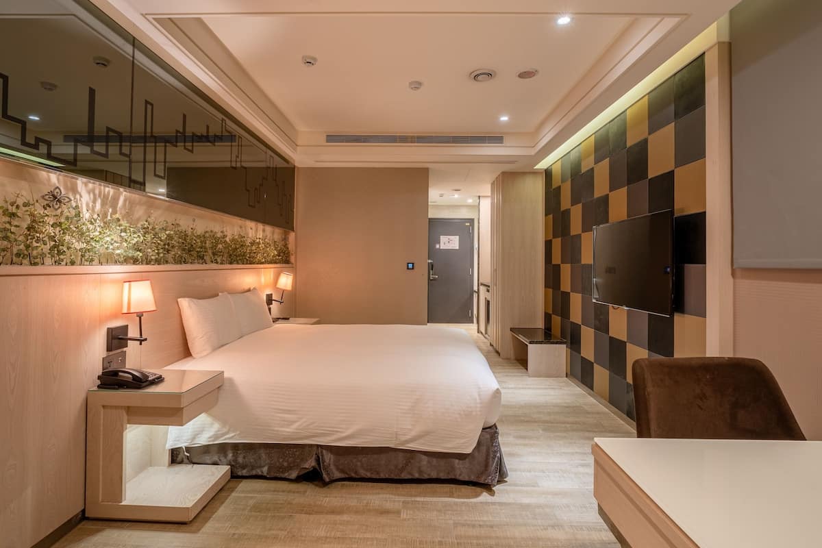 A modern hotel room with a large bed, bedside lamps, a flat-screen TV, and a small desk.