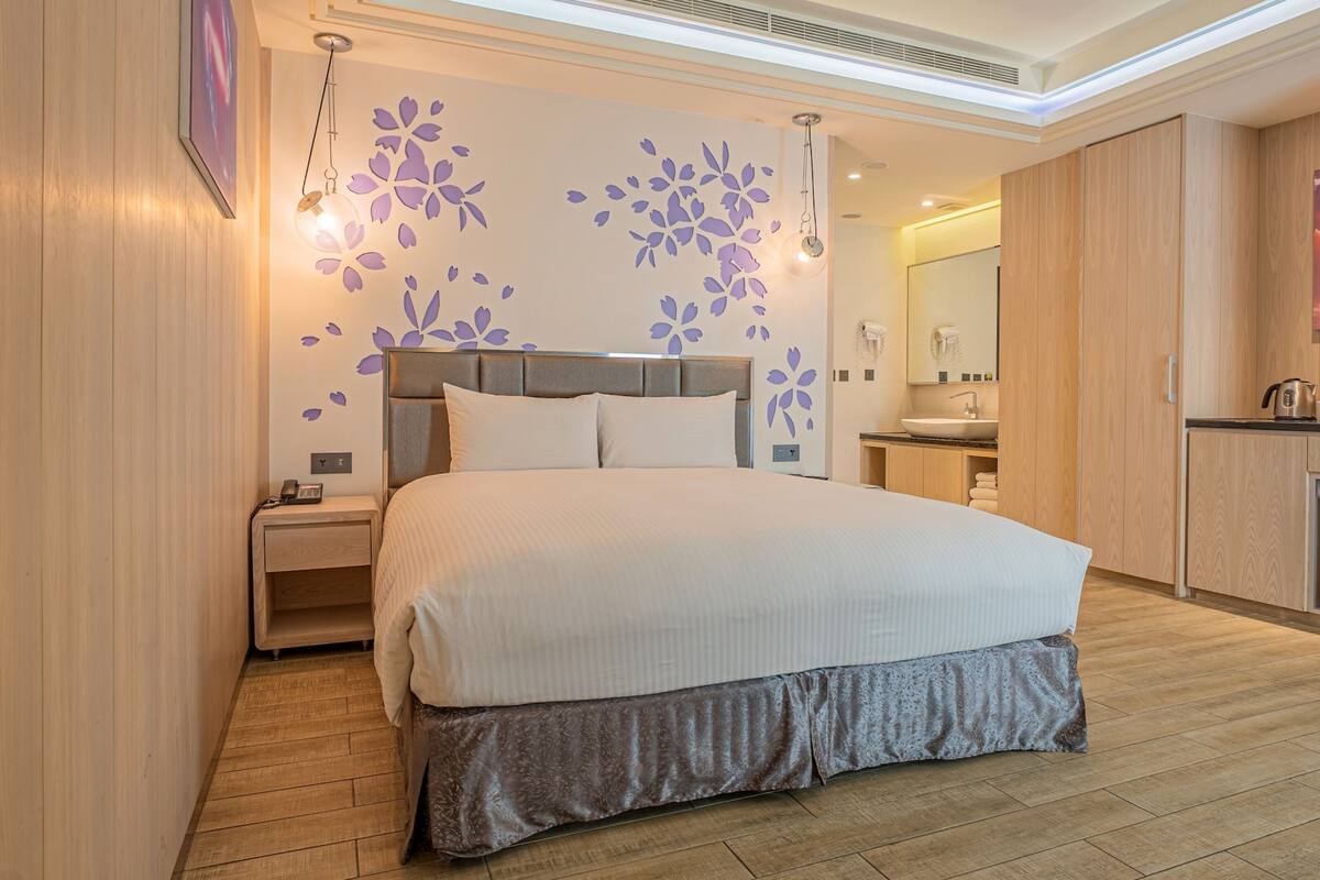 A modern bedroom with a large bed, bedside tables, a built-in wardrobe, and a bathroom with a sink and mirror.
