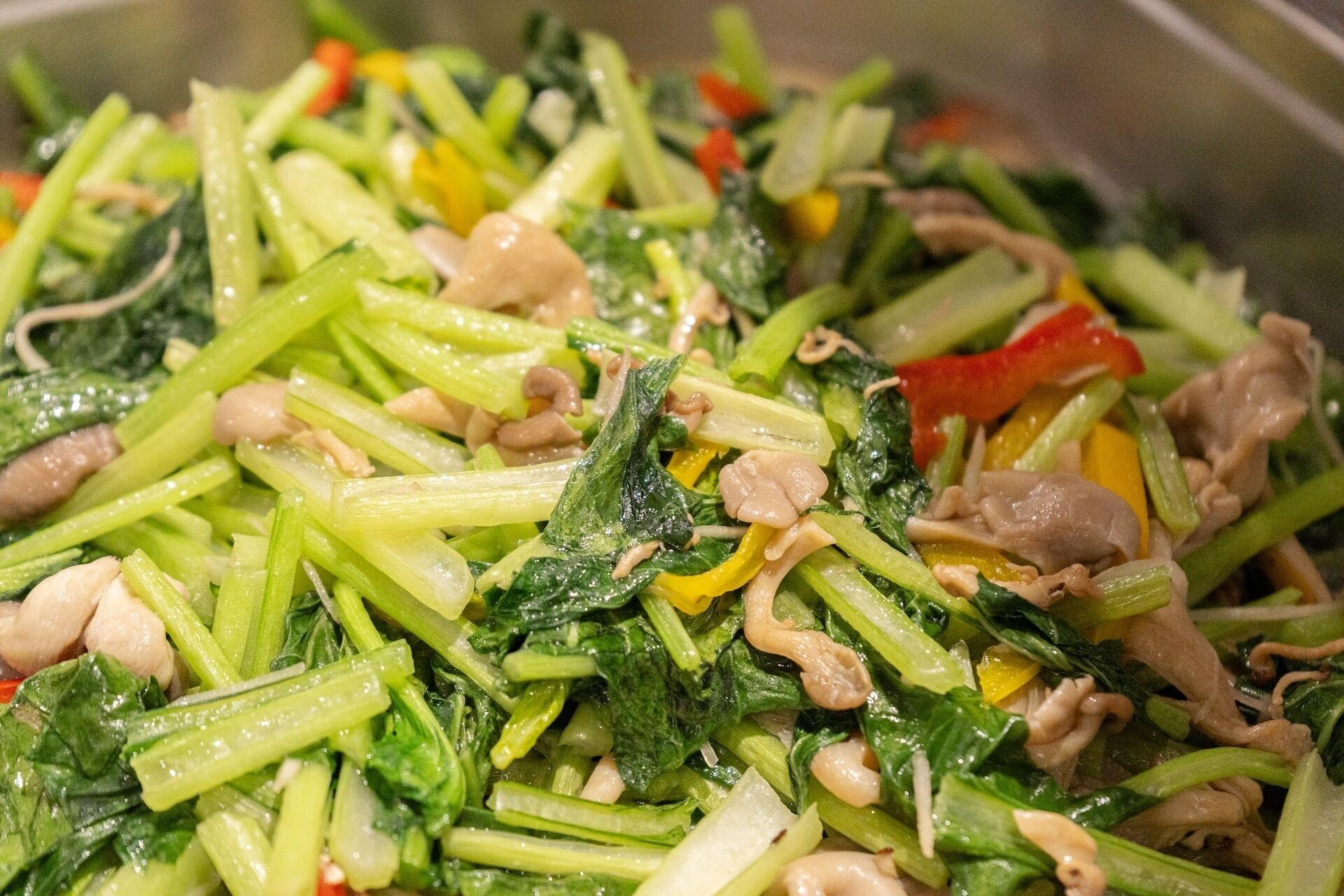 A close-up of a stir-fried vegetable dish with green vegetables, red bell peppers, and chunks of meat.